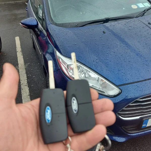 2 car keys in hand in front of blue car