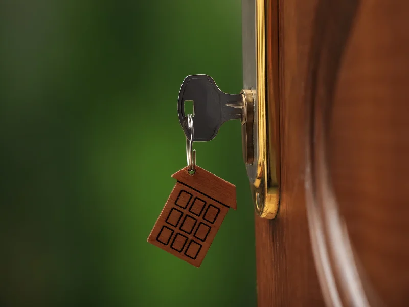 Open door with key on blurred green background, closeup. Space for text